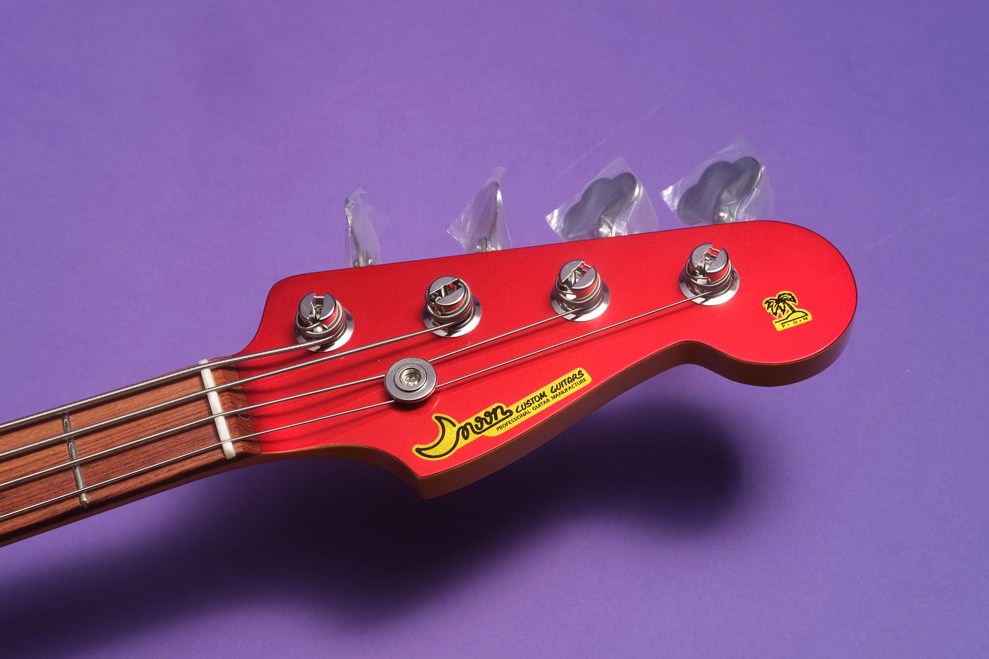 Close-up of a red electric bass guitar headstock with tuning pegs on a purple background